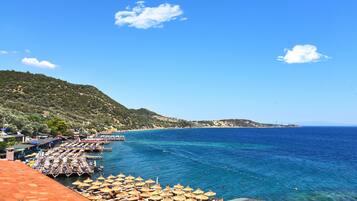 Una zona costera con playa, sombrillas y un muelle.