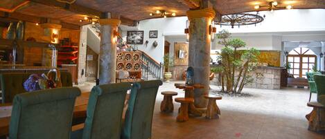 A spacious lobby with wooden furniture, stone pillars, and a staircase leading to upper floors.