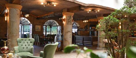 A rustic interior with exposed wooden beams, large columns, and a dining area with green upholstered chairs.