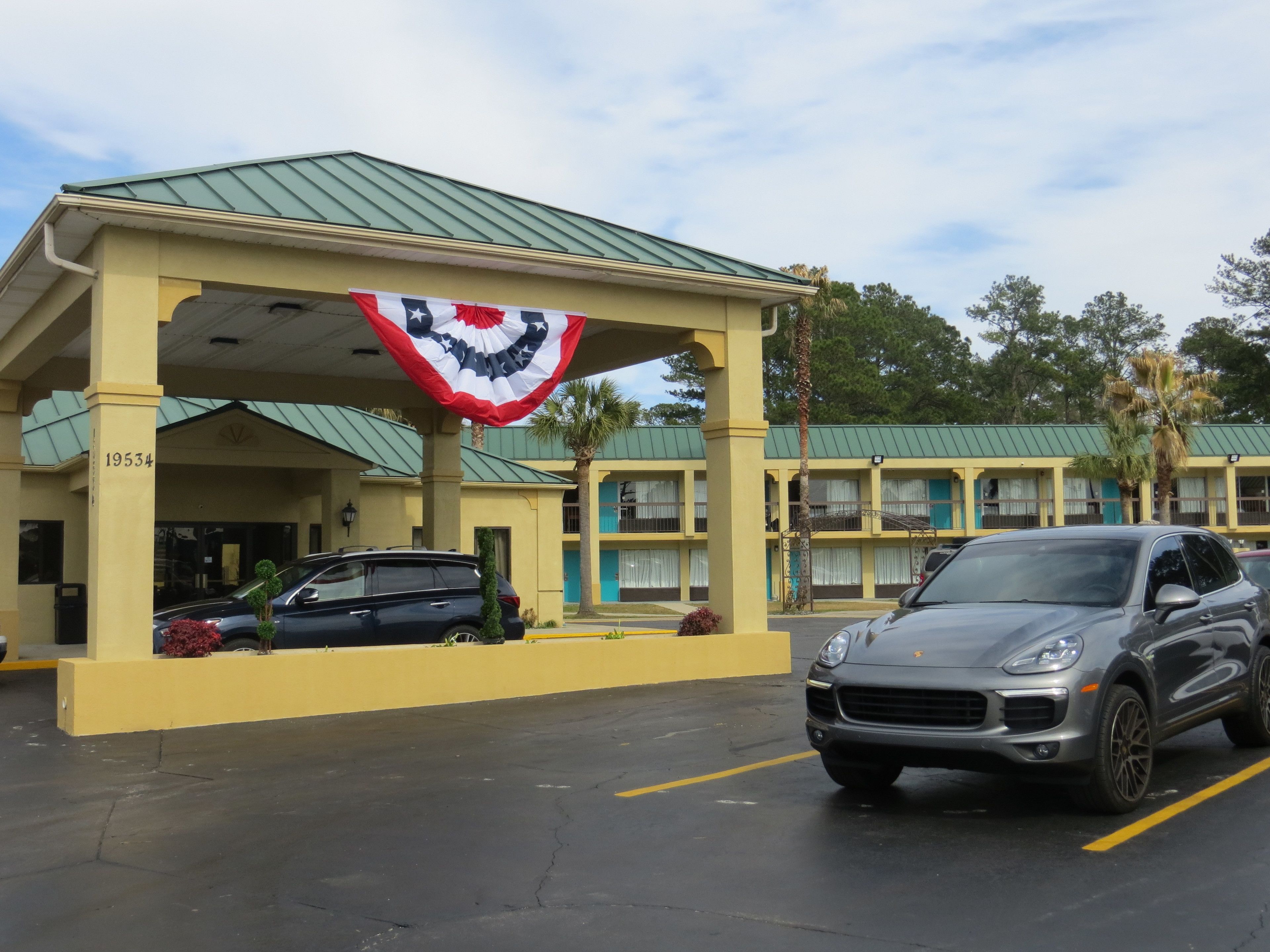 A motel with a green roof, a flag hanging from the entrance, and a parked car.