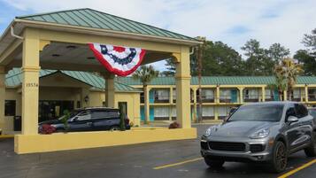 A motel with a green roof, a flag hanging from the entrance, and a parked car.