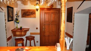 Una zona con barra de madera, con taburetes, un mostrador pequeño de madera y una puerta con marco de madera.