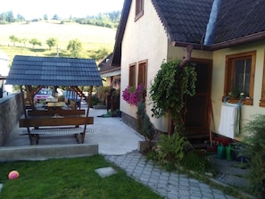 A house with a patio, a covered seating area, and a garden with plants and flowers. - Penzion Leštiny (Leštiny)