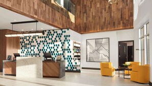 A modern hotel lobby with a wooden reception desk, a hexagonal patterned wall, and a large abstract painting. - Hyatt Place Oklahoma City / Bricktown (Oklahoma City)