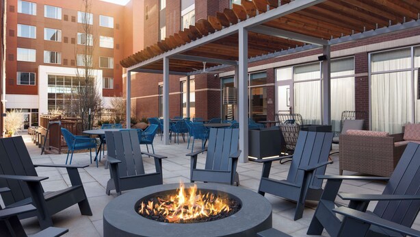 An outdoor seating area with chairs and a fire pit, surrounded by a covered patio and a brick building in the background. - Hyatt Place Oklahoma City / Bricktown (Oklahoma City)