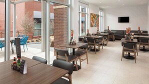 A modern dining area with tables and chairs, a brick wall, and a large window. - Hyatt Place Oklahoma City / Bricktown (Oklahoma City)