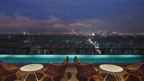 A rooftop pool area with two chairs and a table, overlooking a cityscape at night.