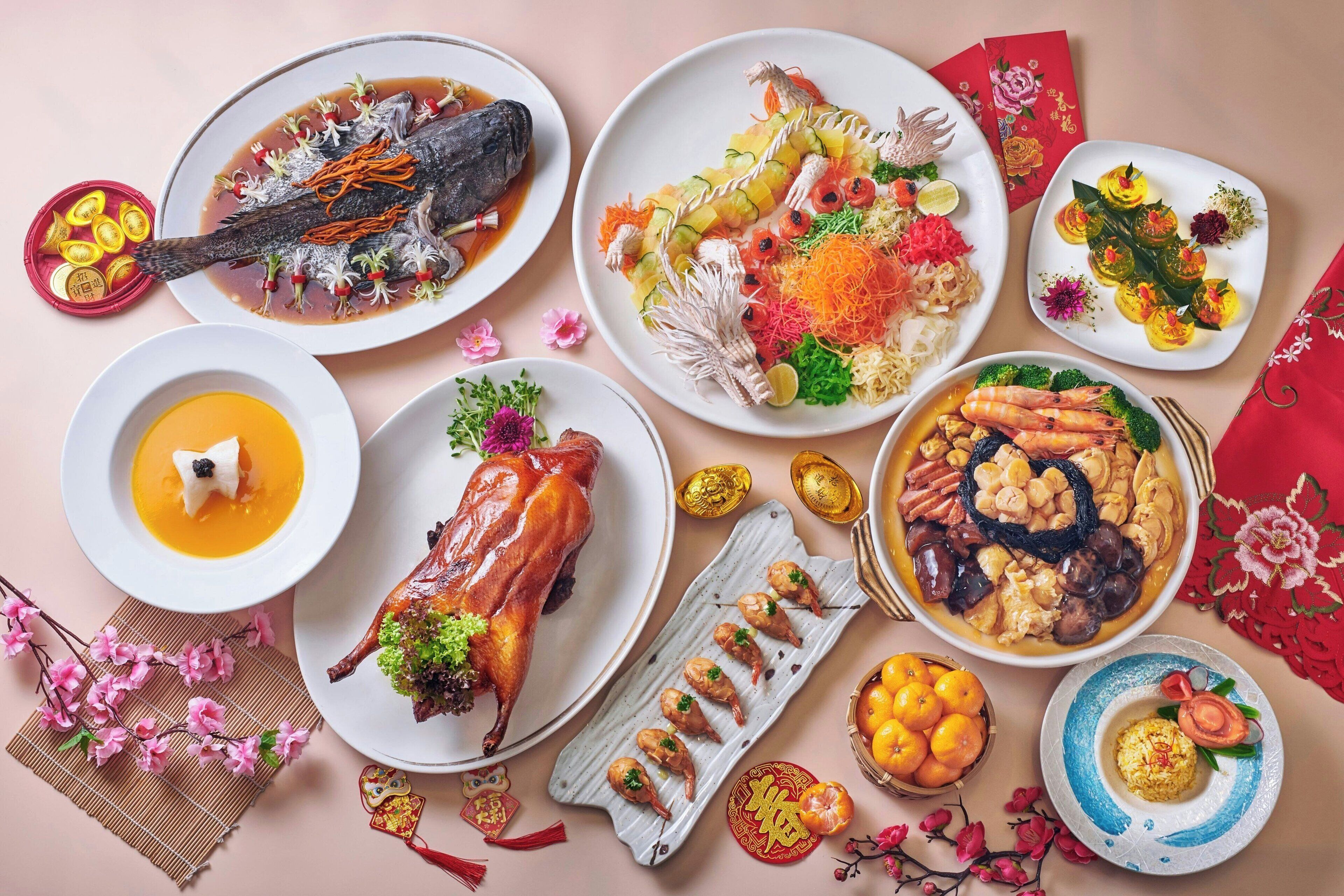 Diverses platillos, incloent un ànec rostit sencer, gambes i un bol de sopa, presentats sobre una taula amb elements decoratius i decoracions tradicionals del nou any xinès.