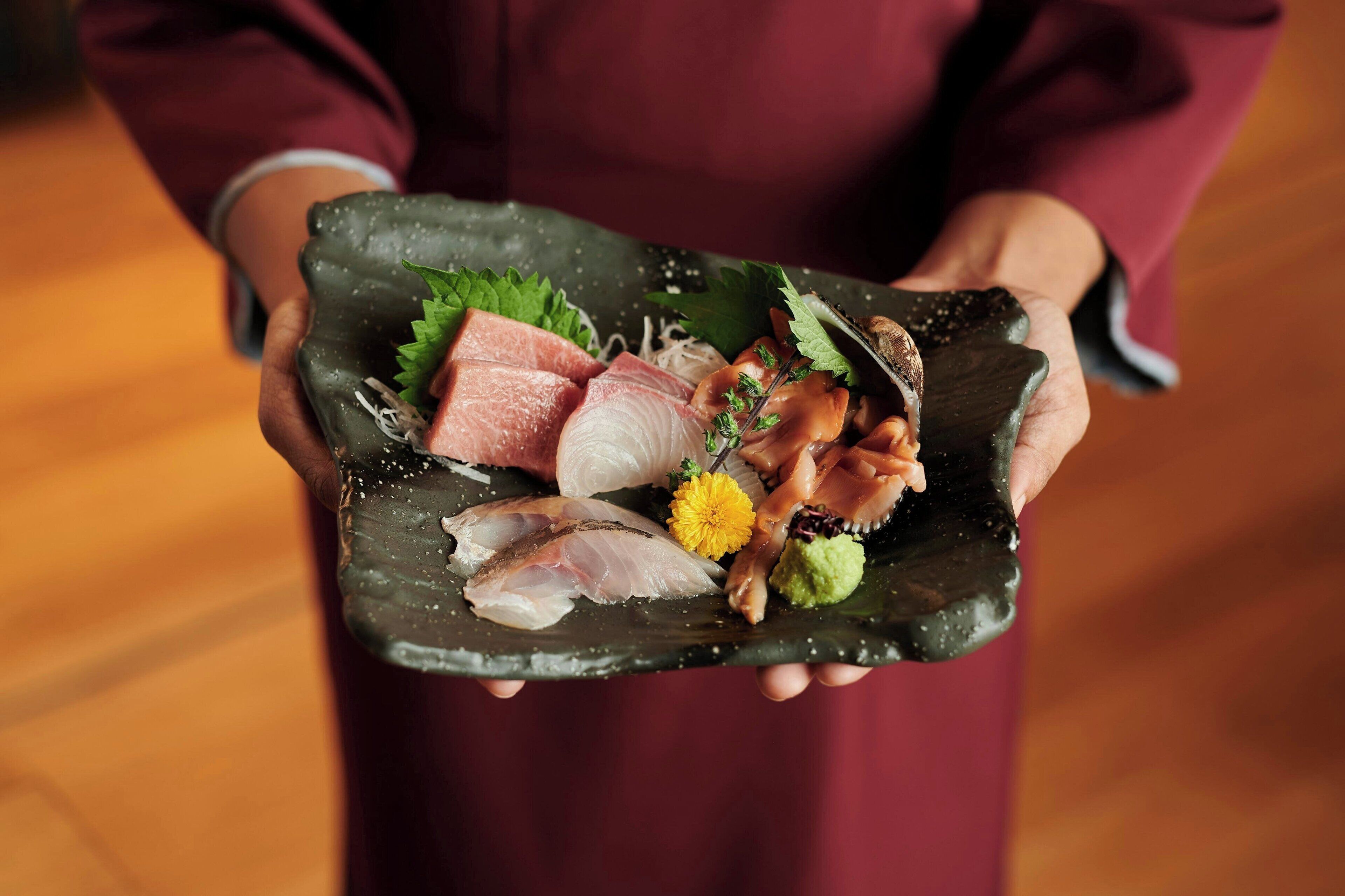 Una persona sosteniendo un plato de cerámica con diferentes tipos de pescado y guarniciones.