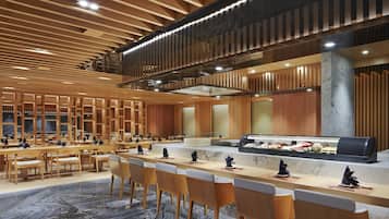 Un amplio vestíbulo de hotel con una larga recepción, varias áreas de descanso y un diseño moderno con paneles de madera y suelo de mármol.