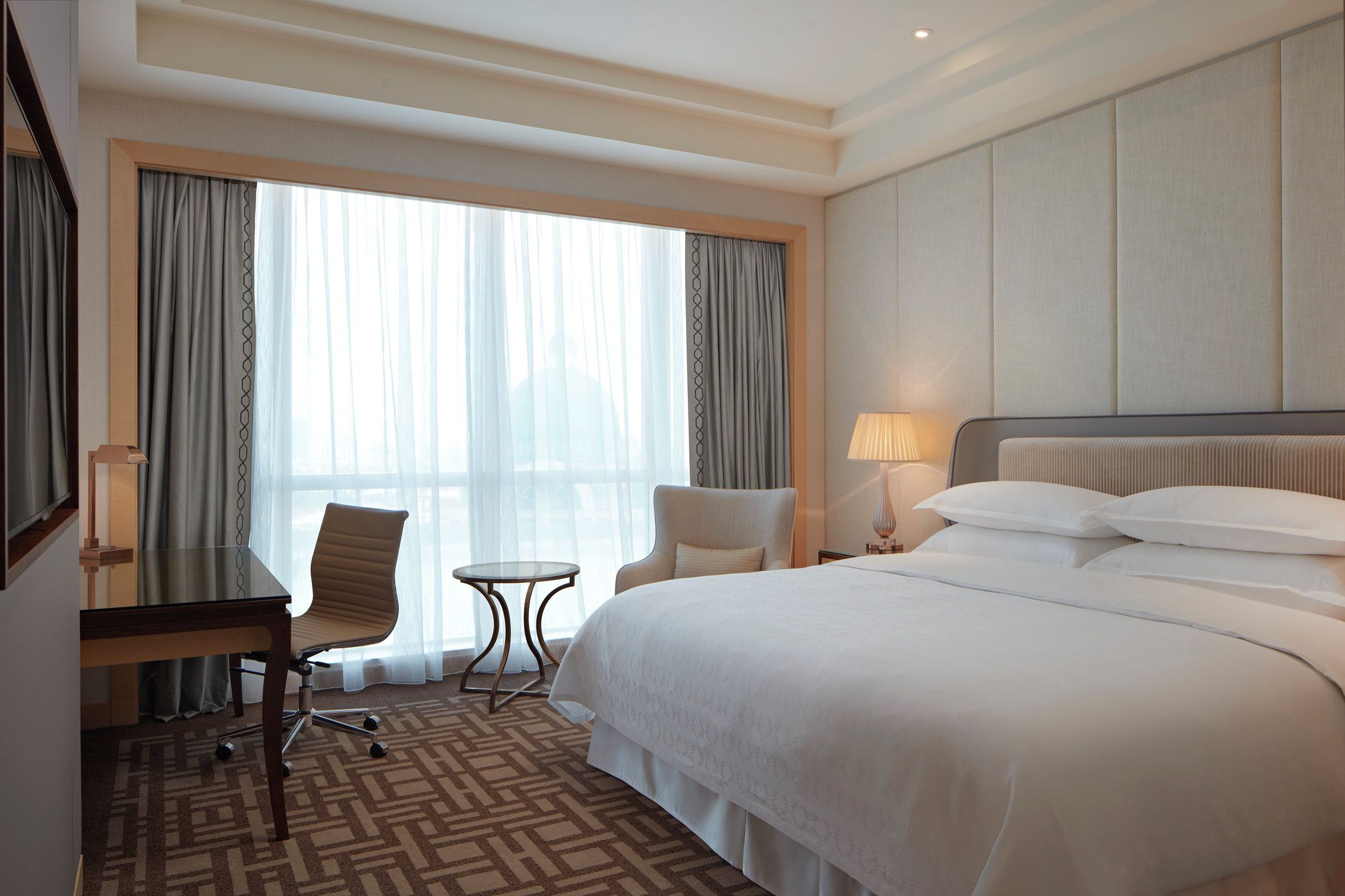 Una habitación de hotel con una cama, dos sillas, una mesita y un escritorio.