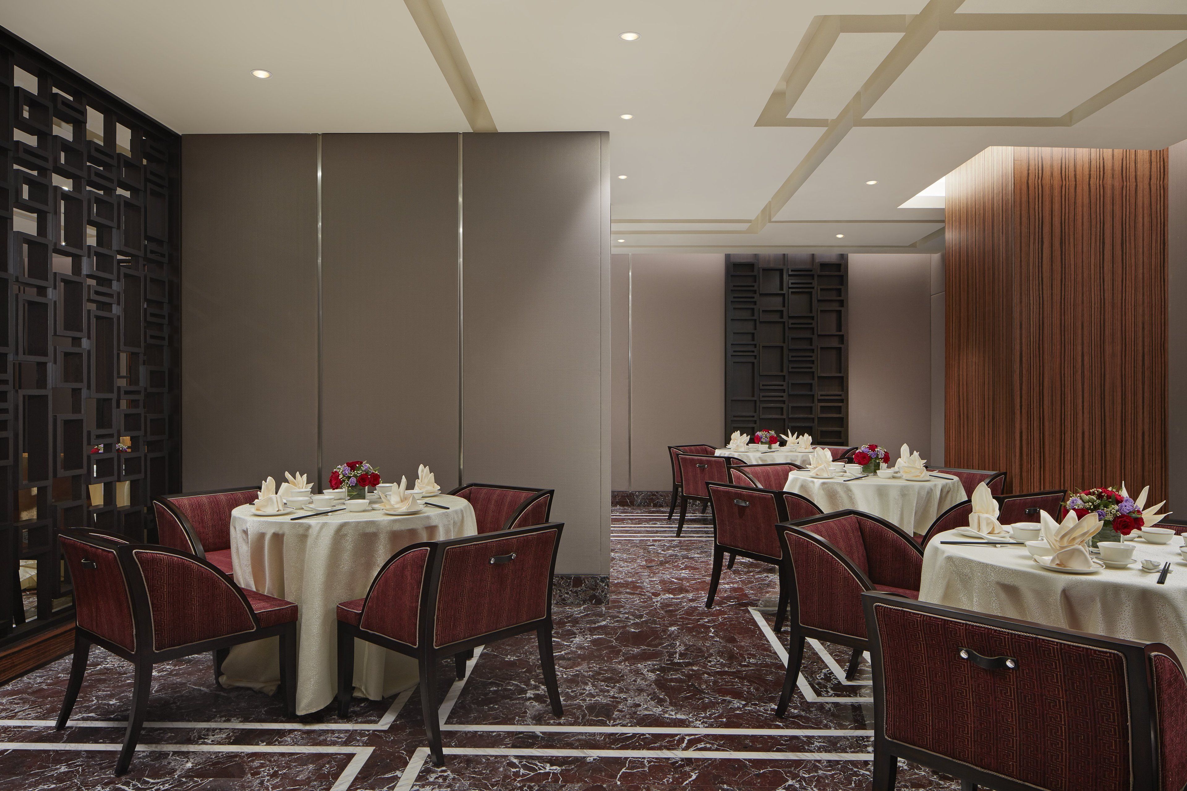 A dining area with round tables, red upholstered chairs, and a marble floor.