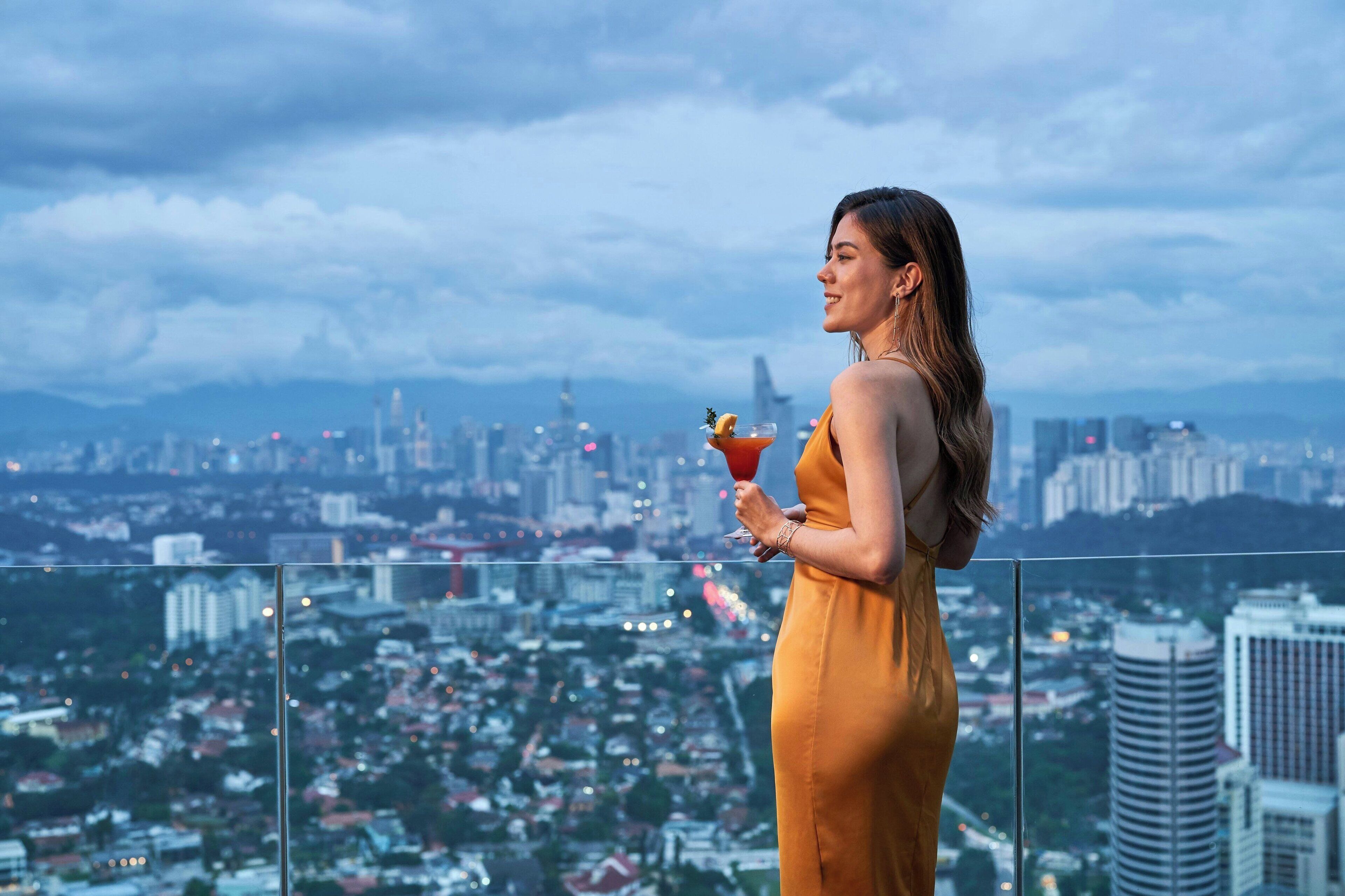 Una persona con un abito giallo in piedi su un balcone con vista sulla città.