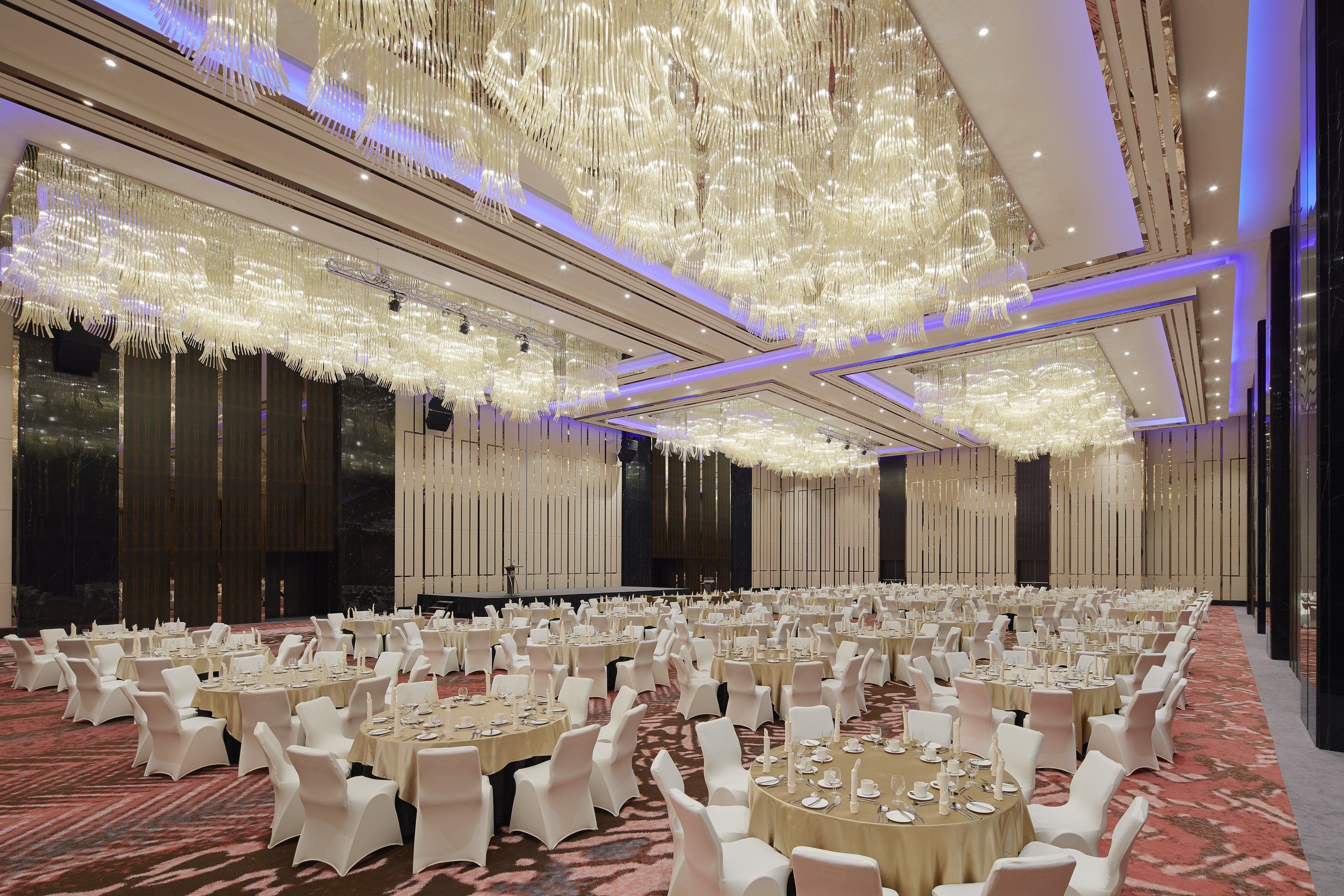 Un salón de banquetes con mesas redondas, sillas blancas y una araña.