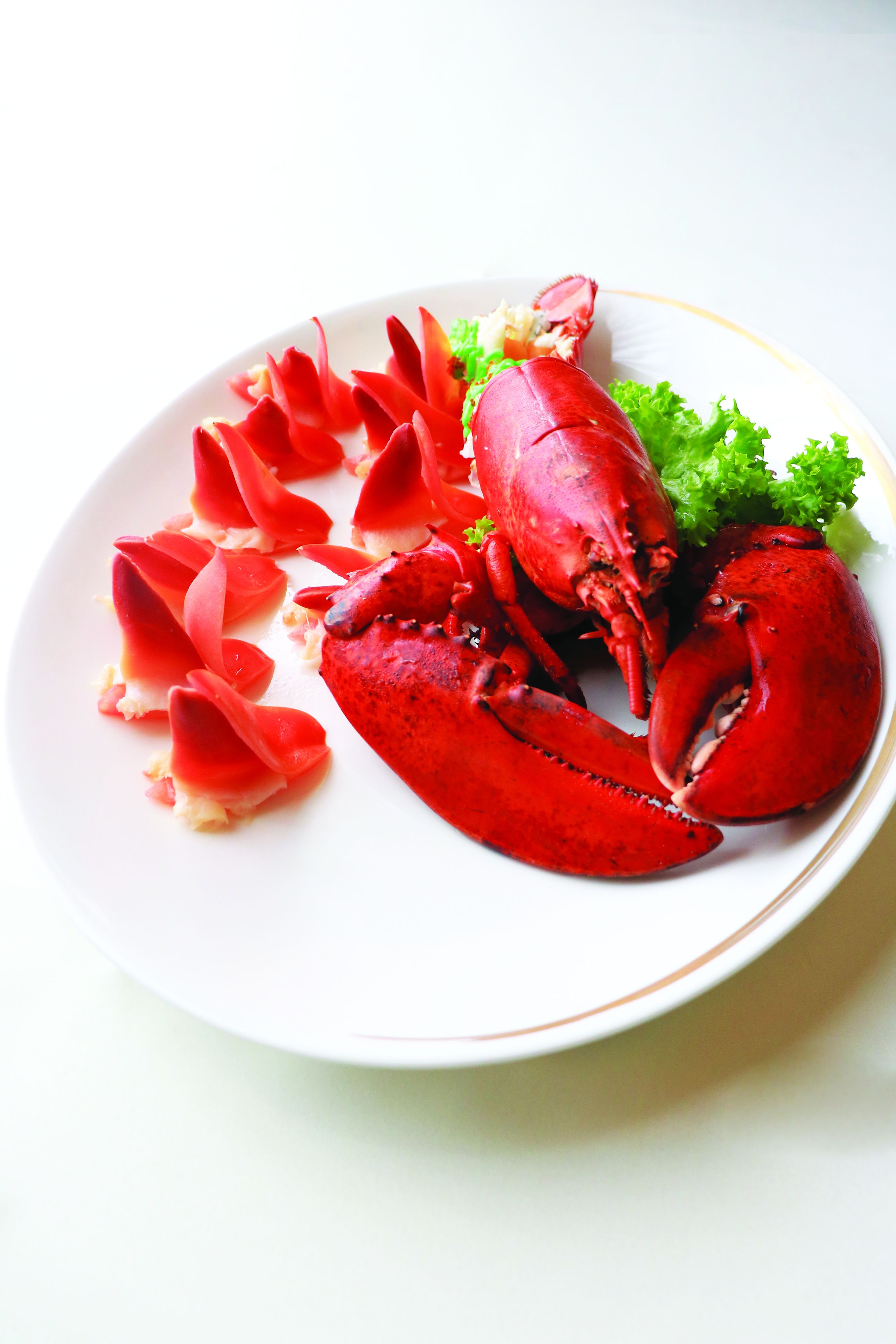 Une assiette contenant un homard cuit et quelques tranches de légumes rouges.