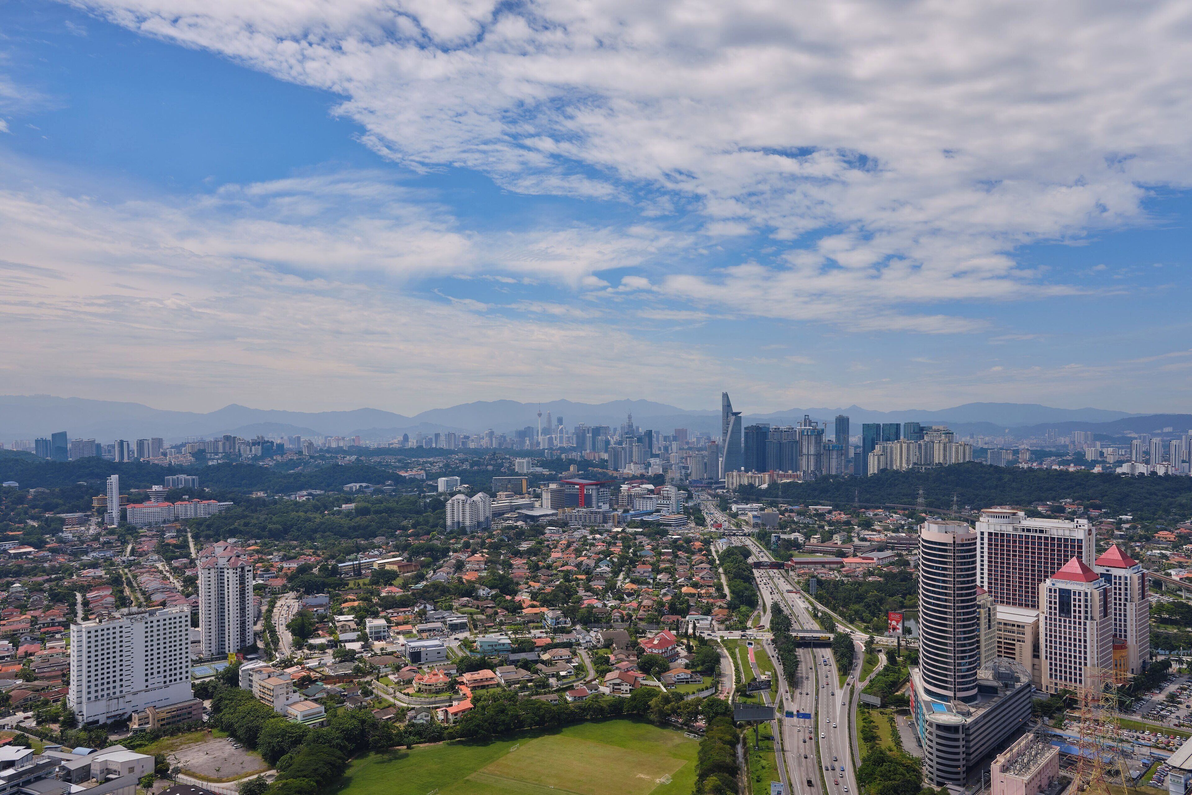 A cityscape with high-rise buildings, a highway, and a green park area.