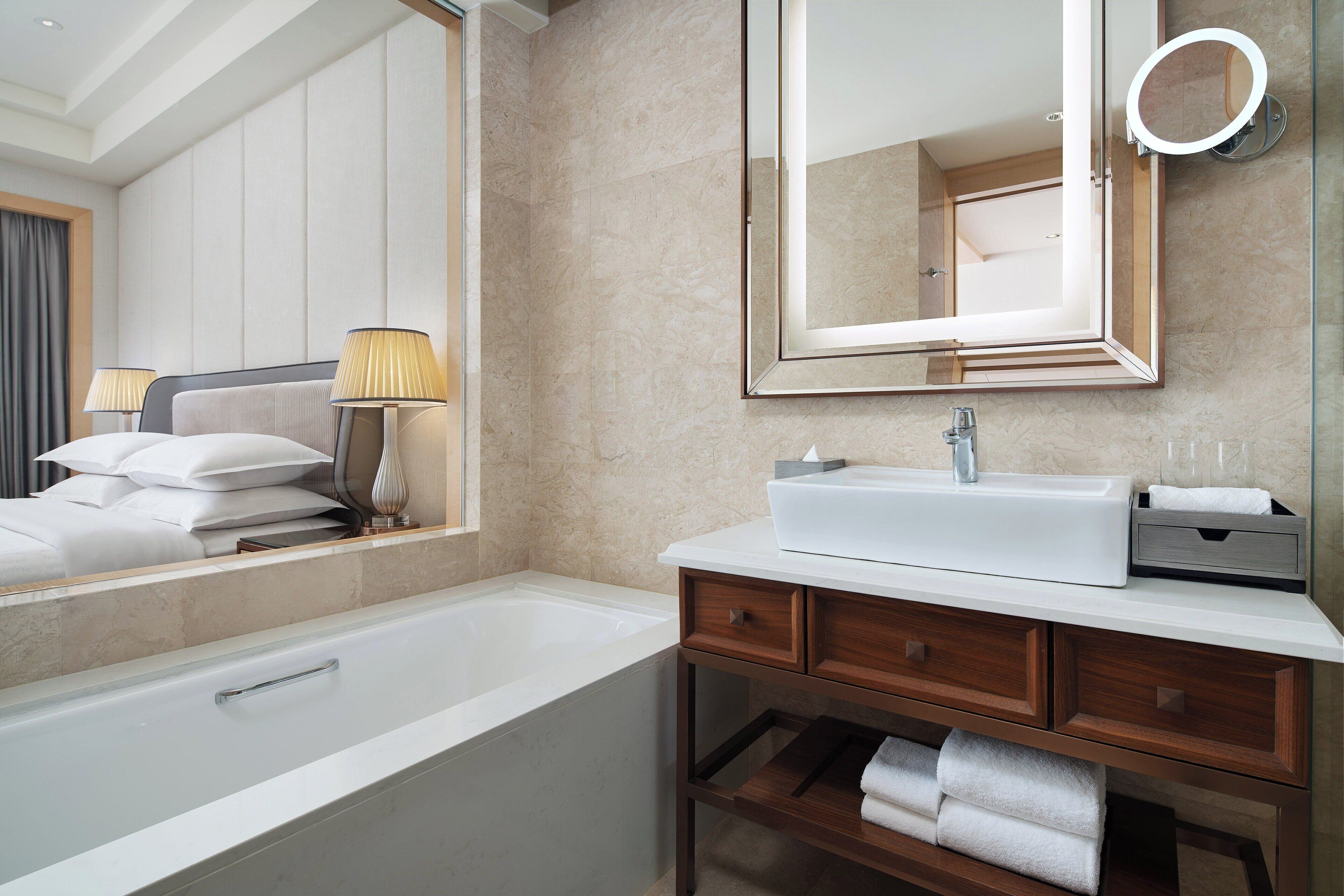 Une salle de bain moderne avec une baignoire, un grand miroir, un meuble-lavabo et un porte-serviettes.