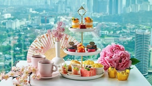 A dessert tray with various sweets and a fan, a pink flower, and a cup on a table with a city view in the background.