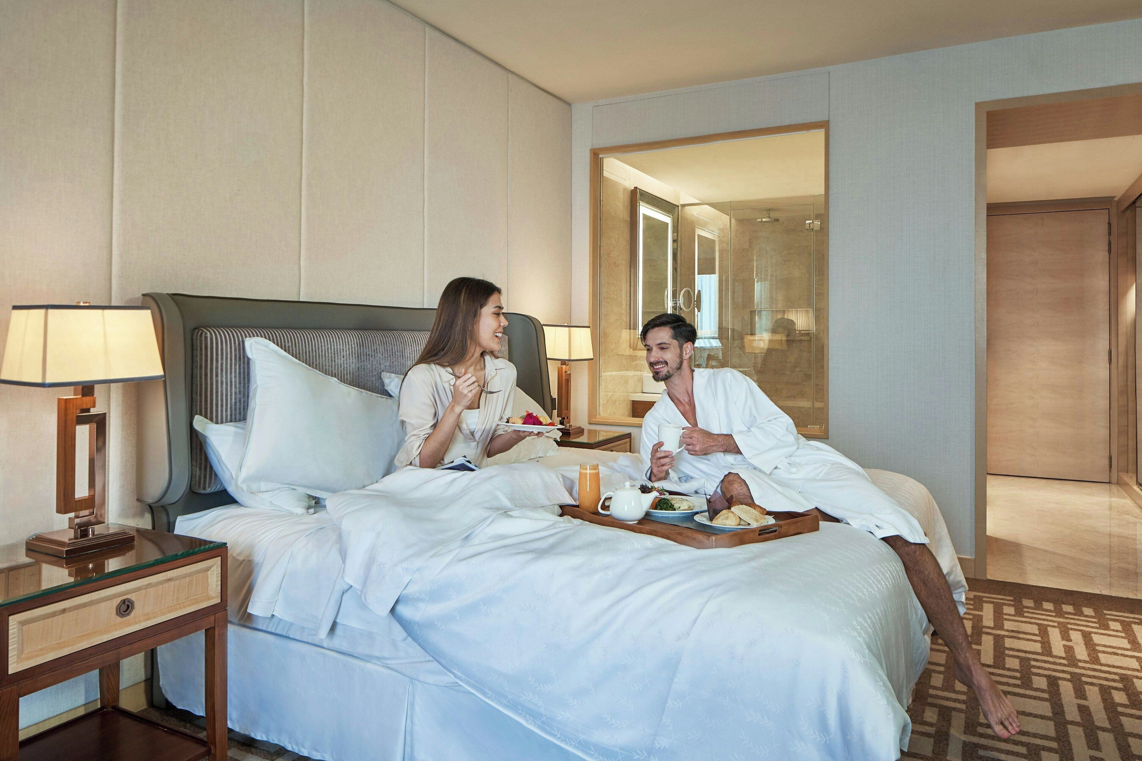 A hotel room with a bed, bedside tables, a tray with breakfast items, and a mirror.