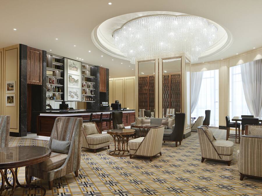 A spacious lobby with a bar area, seating arrangements, and a large chandelier.
