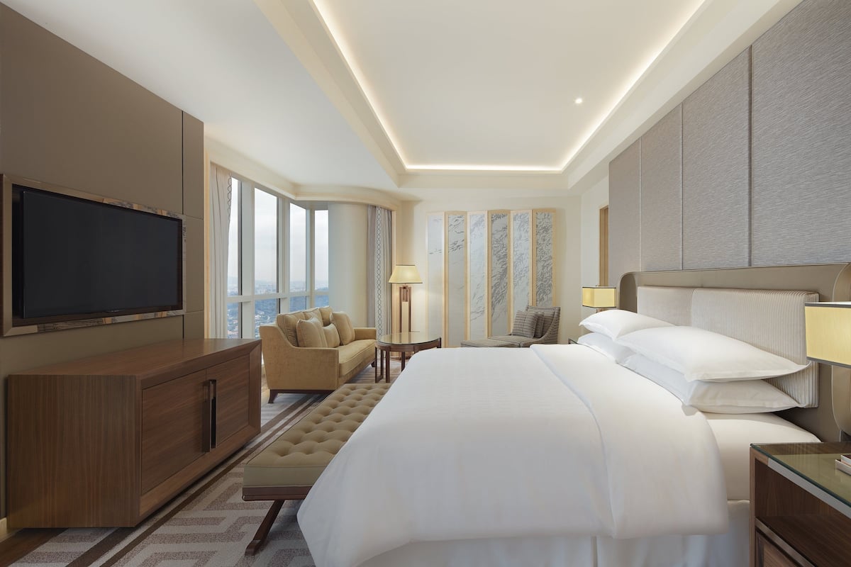 A hotel room with a large bed, a TV, a sofa, a desk, and a view of the city.