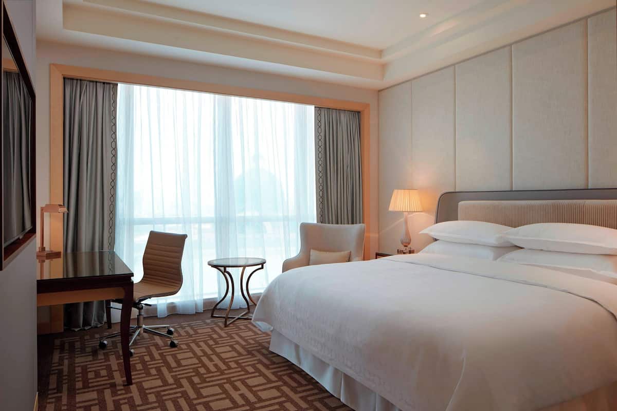 A hotel room with a large bed, a desk, a chair, and a small table.