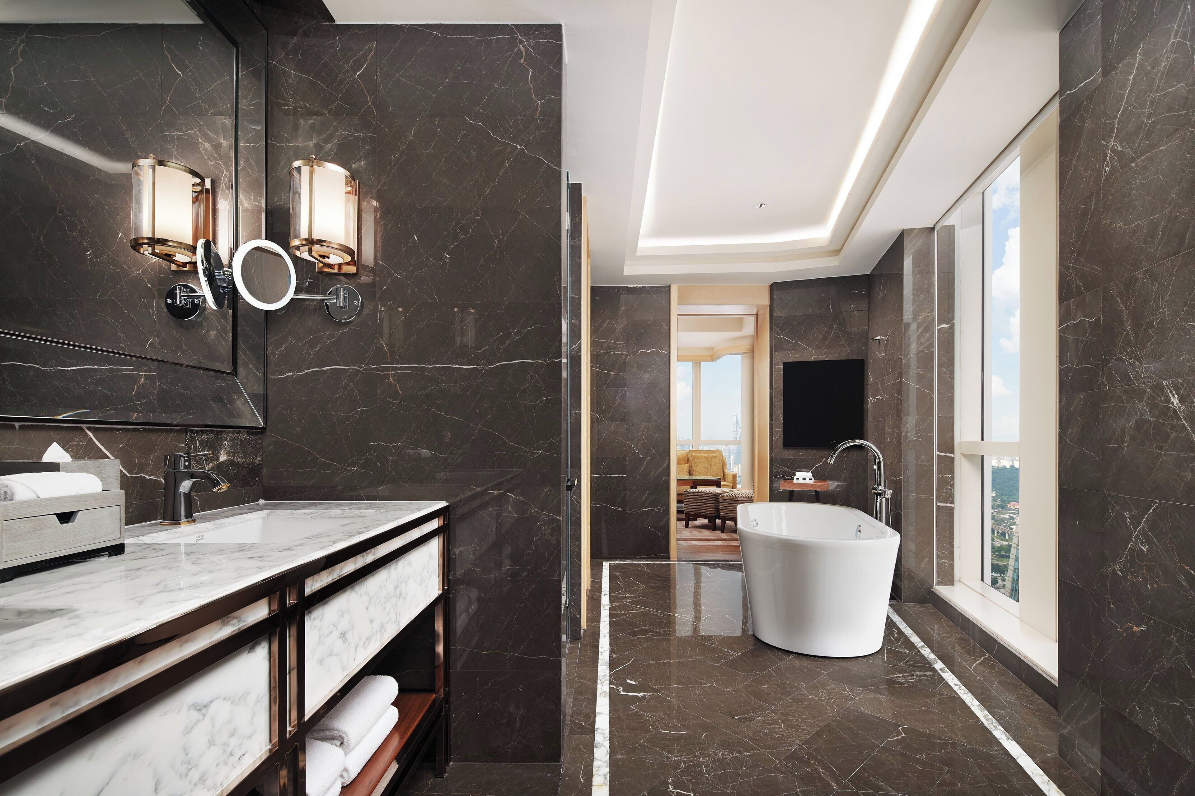 A modern bathroom with a large mirror, two wall-mounted lights, a freestanding bathtub, and a vanity with a sink and towel rack.