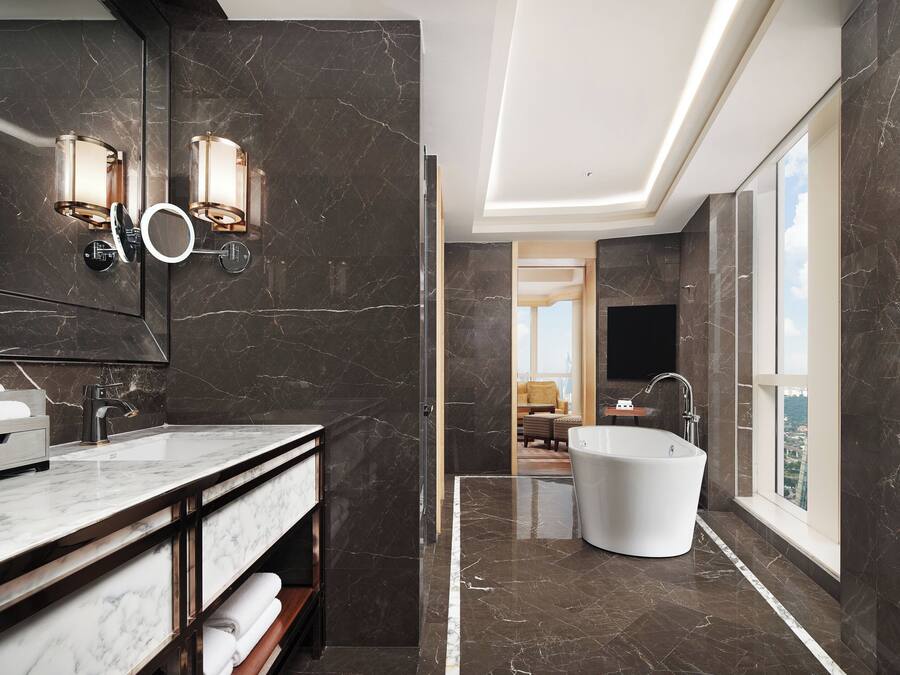 A modern bathroom with a large mirror, two wall-mounted lights, a freestanding bathtub, and a vanity with a sink and towel rack.
