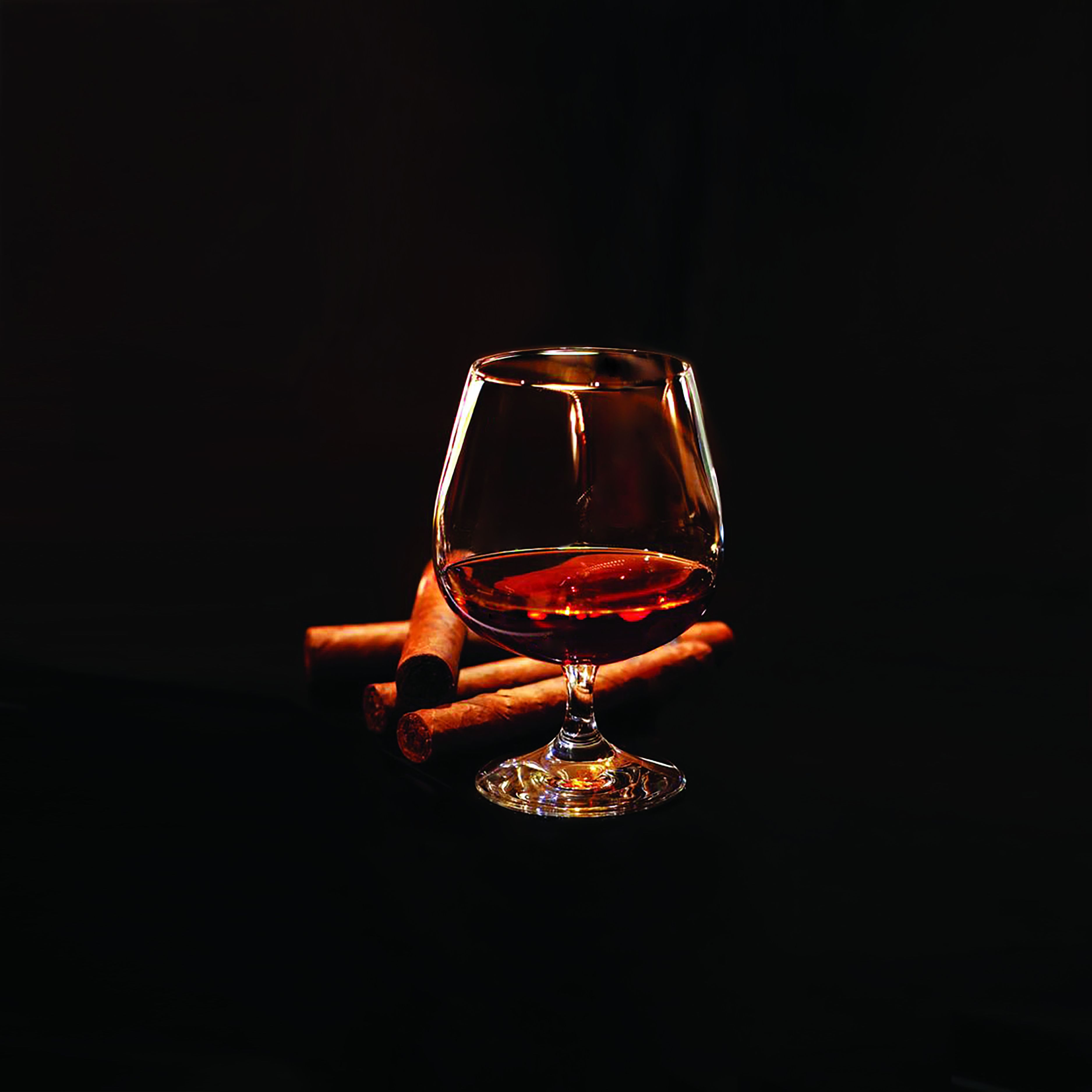 Een glas rode wijn met een steel, geplaatst op een donker oppervlak met twee sigaren ernaast.