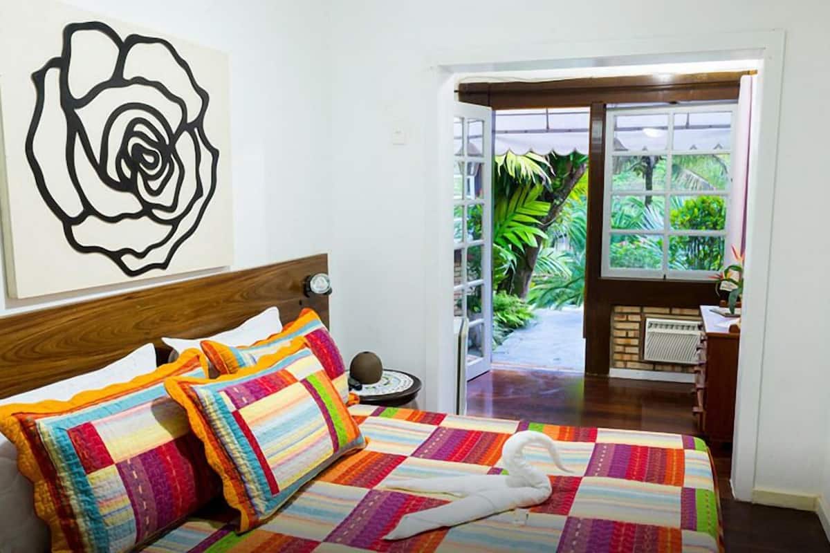 Een slaapkamer met een houten hoofdbord, een kleurrijke quilt en een groot kunstwerk van een zwarte roos aan de muur.