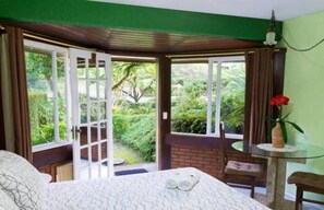Una habitación con cama, una mesa de vidrio y vistas a la vegetación a través de puertas abiertas.
