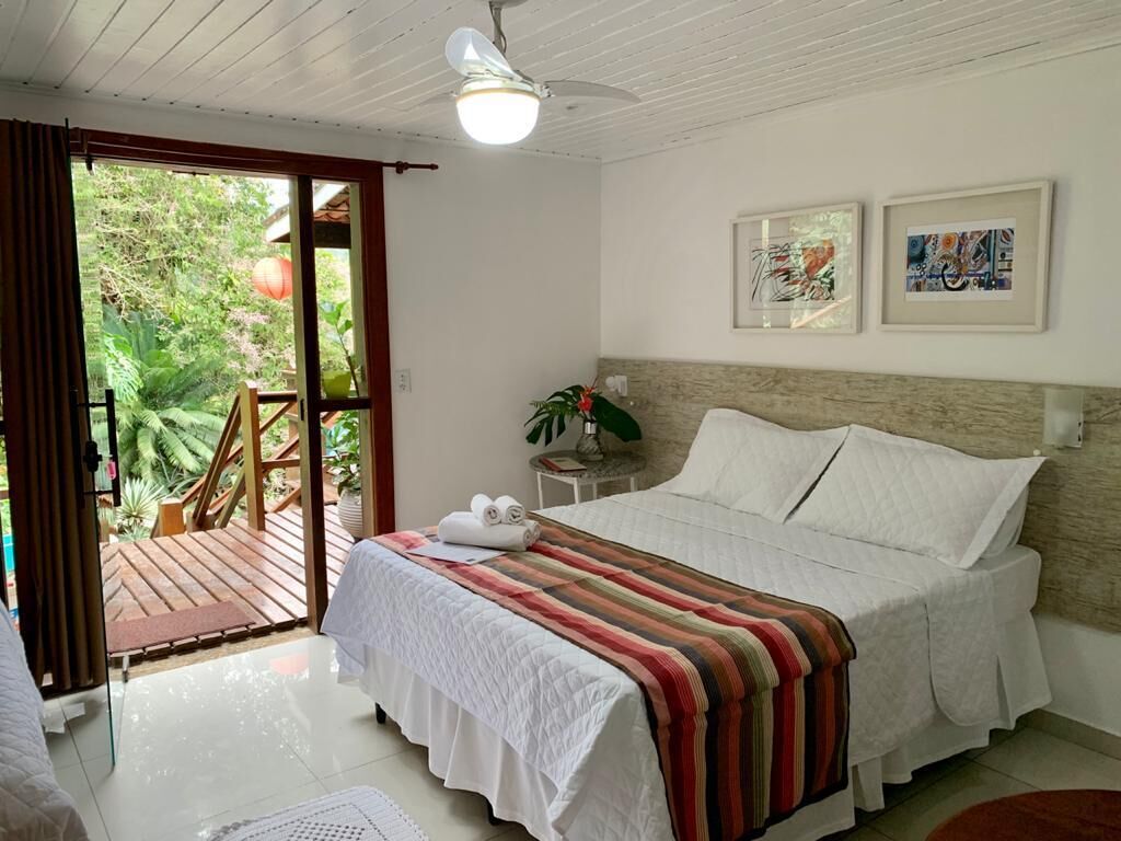 Quarto com cama, mesa de cabeceira, ventoinha no teto e vista para o exterior.