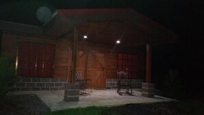 A wooden house with a porch, two chairs, and a small table. - Cabañas San Isidro (La Fortuna)