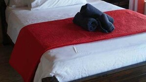 A hotel room with a wooden bed, white linens, a red blanket, and a rolled-up towel on the bed. - Cabañas San Isidro (La Fortuna)