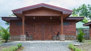 A rustic wooden building with a large wooden door, two chairs outside, and a gravel driveway. - Cabañas San Isidro (La Fortuna)