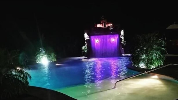 A nighttime swimming pool with a waterfall feature and illuminated surroundings. - Cabañas San Isidro (La Fortuna)