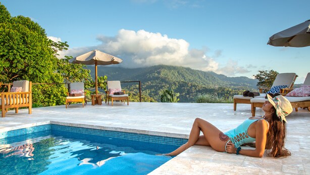 Zona de piscina con sillones reclinables y sombrillas, con vistas a un paisaje montañoso.