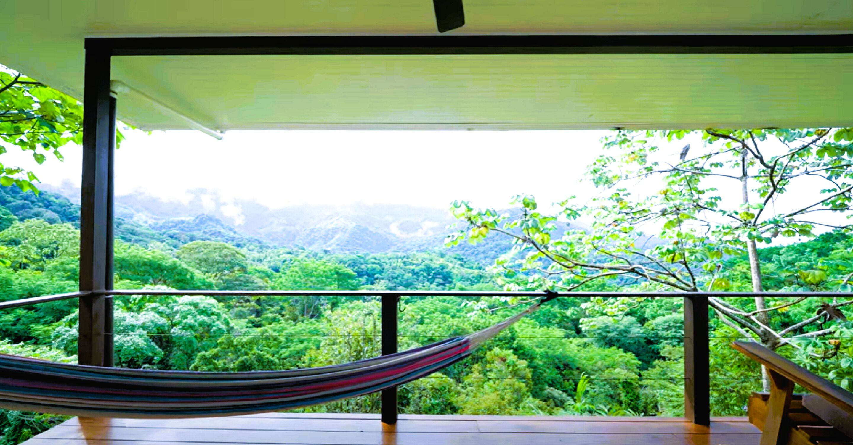 A hammock on a balcony with a view of a lush green forest and mountains.