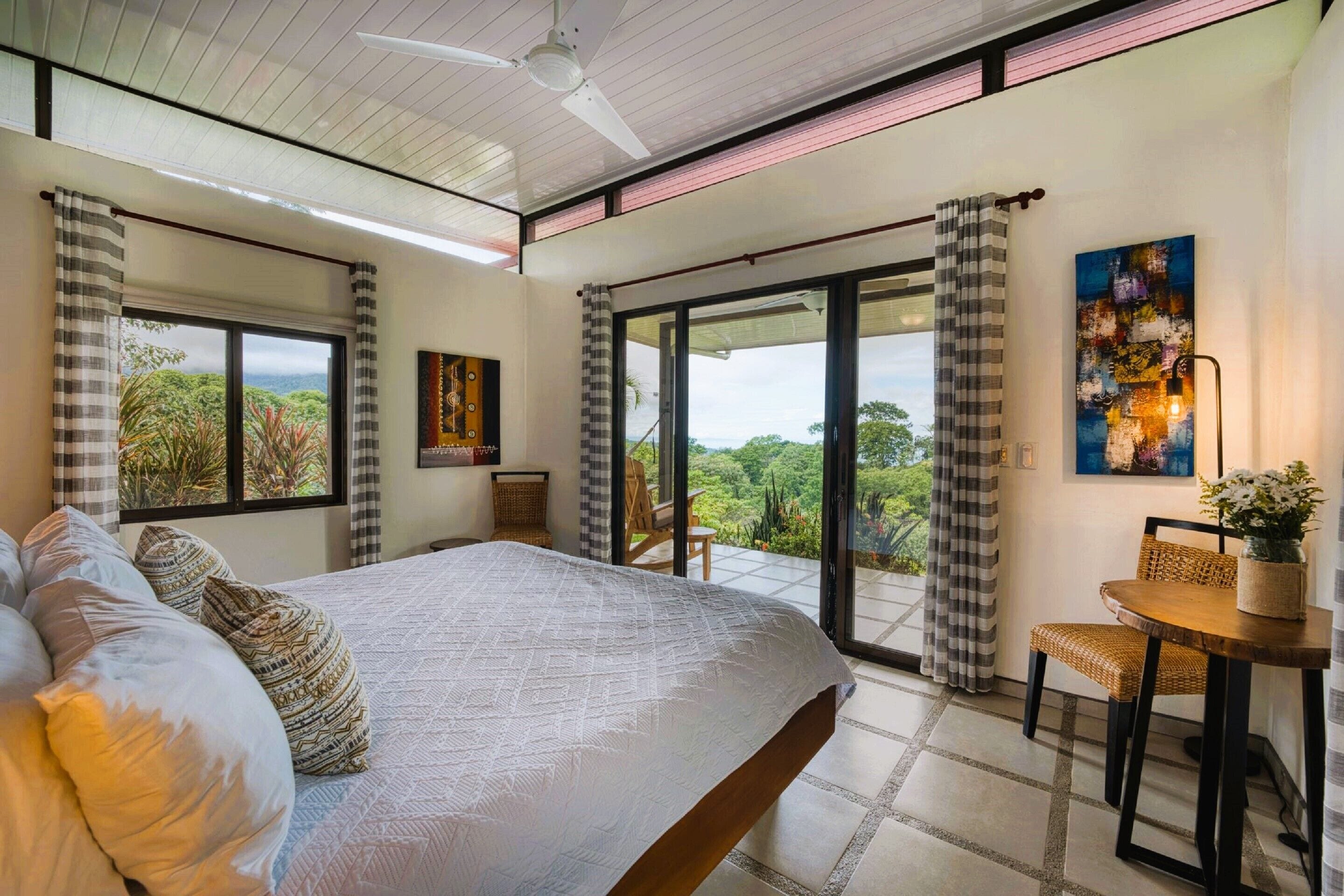 A bedroom with a large bed, a dining area with a table and chairs, and a balcony with curtains.