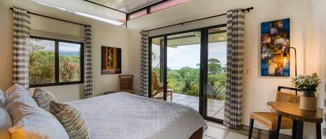 A bedroom with a large bed, a dining area with a table and chairs, and a balcony with curtains.