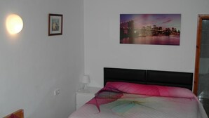 A bedroom with a bed, a nightstand, a wall-mounted picture, and a window. - Fornet (Altea)