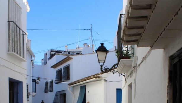 A narrow cobblestone alleyway between white buildings with blue doors and windows. - Fornet (Altea)
