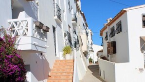 A narrow street with white buildings, a wooden staircase, and a potted plant. - Fornet (Altea)