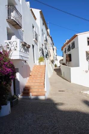 A narrow street with white buildings, a wooden staircase, and a potted plant. - Fornet (Altea)