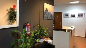 A reception area with a fire extinguisher, potted plants, a desk, and framed pictures on the wall. - Fornet (Altea)