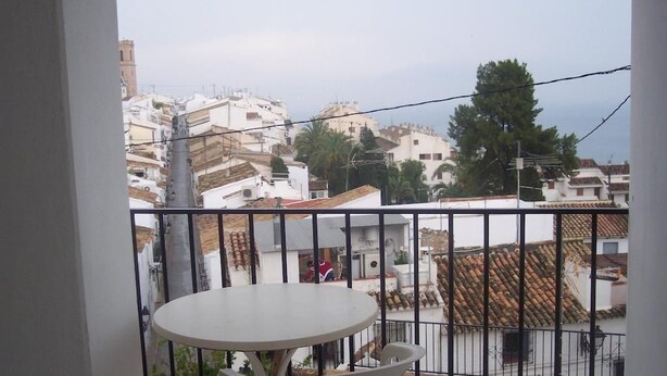 A balcony with a round table and chairs, overlooking a residential area with white buildings and a palm tree. - Fornet (Altea)
