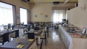 Un espace repas comprenant plusieurs tables et chaises, un lustre et un buffet.