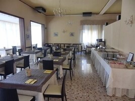 Zona pranzo con diversi tavoli e sedie, un lampadario e un'area buffet.