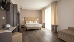 Une chambre d’hôtel avec un lit, un bureau, une chaise, une télévision et une fenêtre avec des rideaux.