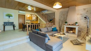 A modern living room with a sofa, coffee table, fireplace, and staircase leading to a kitchen. - Villa Peonia & Villa Ortansia (Mylopotamos)